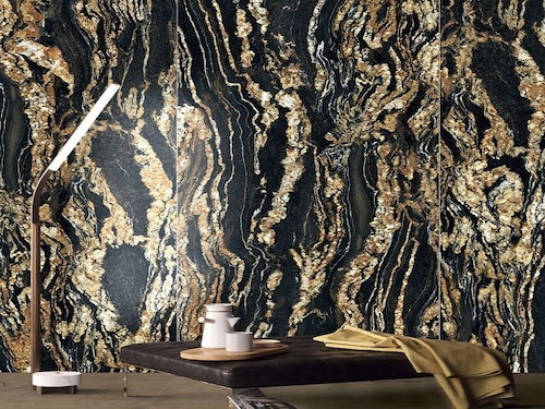 Ściana z płytek Ariana Nobile Black Taurus, czarna powierzchnia z mocnym złoto-beżowym użyleniem, aranżacja z lampą podłogową i siedziskiem.